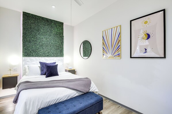 Un dormitorio moderno con una cama, un banco, una pared verde y dos obras de arte enmarcadas.