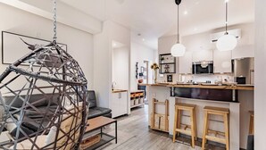 A modern kitchen with a hanging light, a dining area with a hanging chair, and a visible staircase.