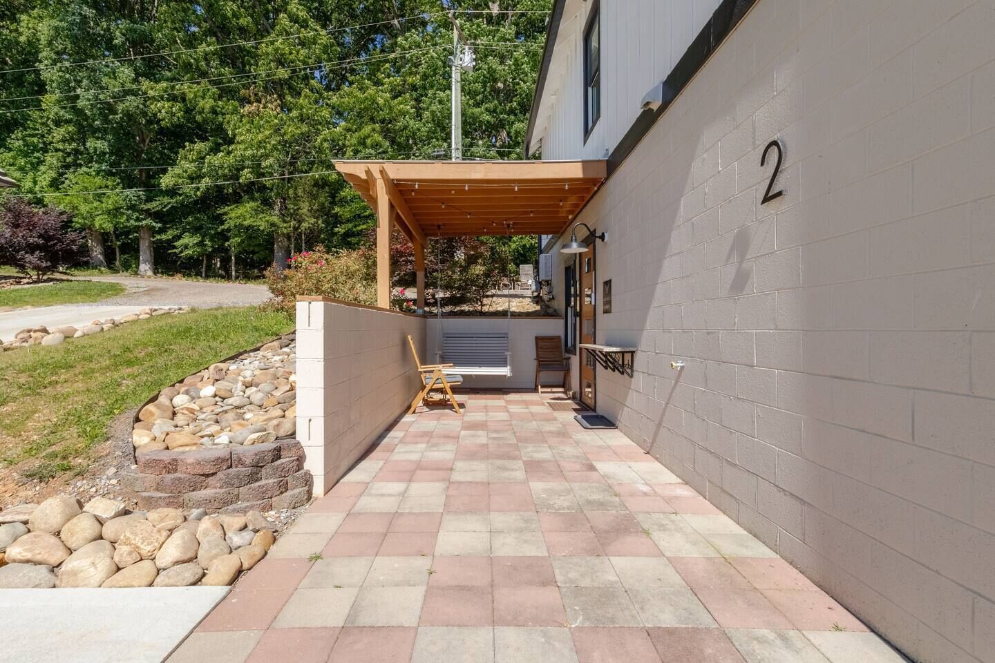 Un espacio exterior cubierto con un sendero pavimentado, una pérgola de madera y un edificio con pared de ladrillo y un letrero con el número 2.