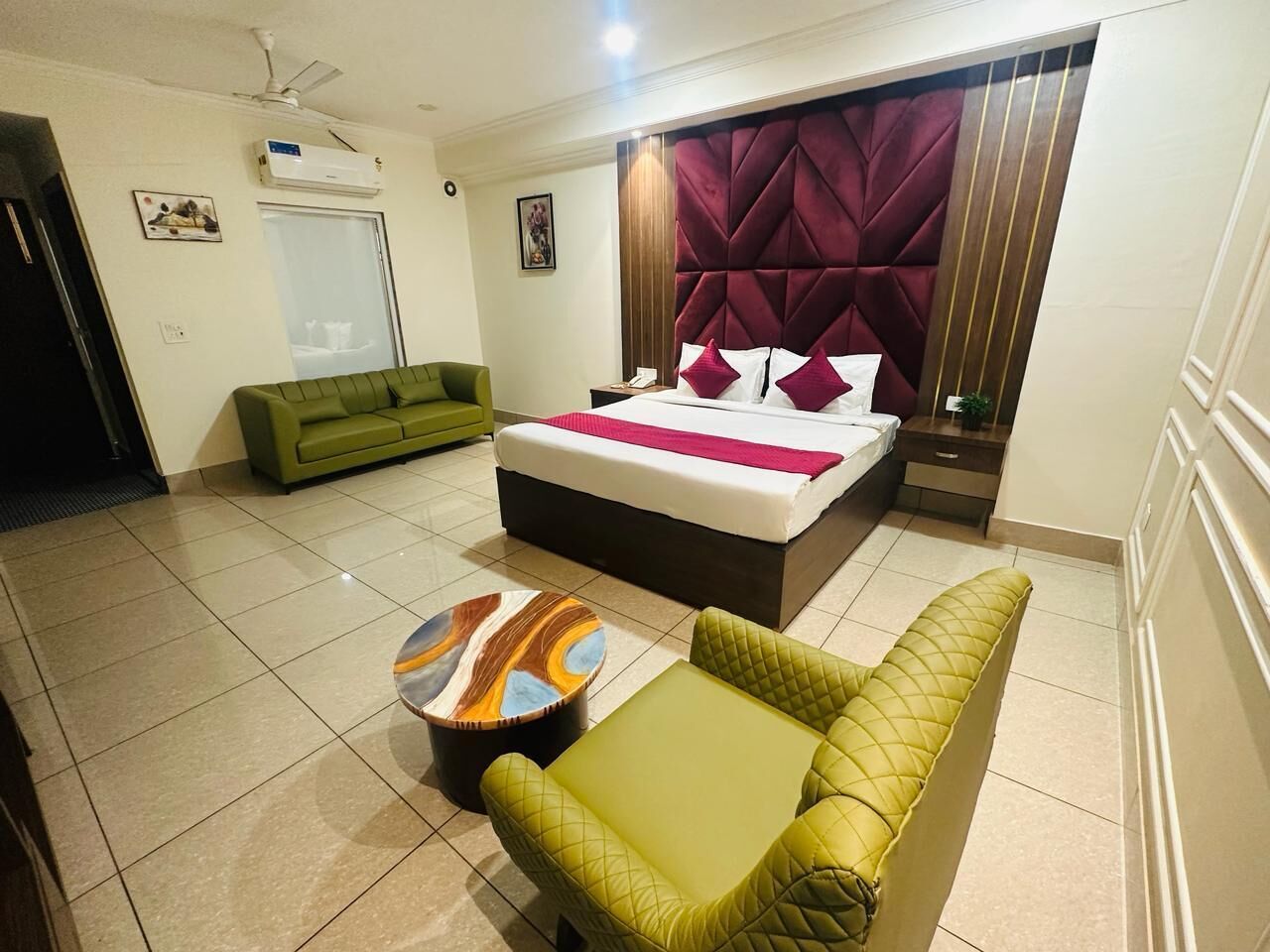 Una habitación de hotel con cama, sofá verde, una mesita pequeña y un cabecero decorativo.