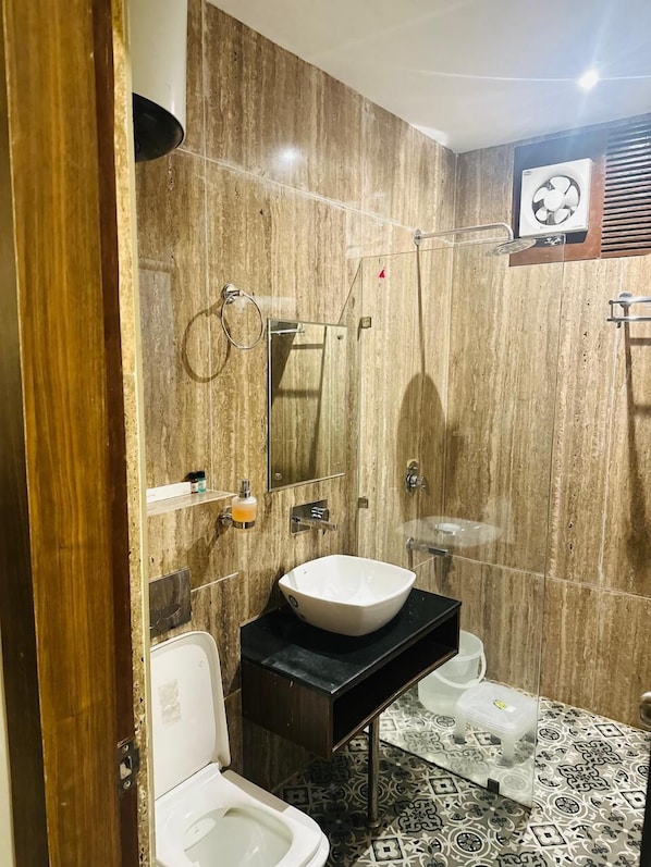 A bathroom with a marble wall, a white sink, a toilet, and a shower area. - Hotel Fortune Ganga (Haridwar)