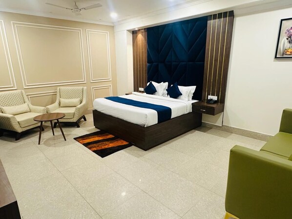 A hotel room with a large bed, a sofa, a small table, and a nightstand. - Hotel Fortune Ganga (Haridwar)