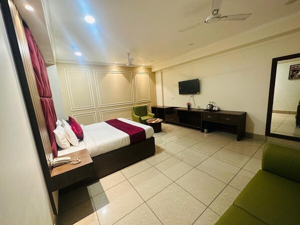 Habitación de hotel con una cama grande, un escritorio, una silla, un televisor y un espejo.
