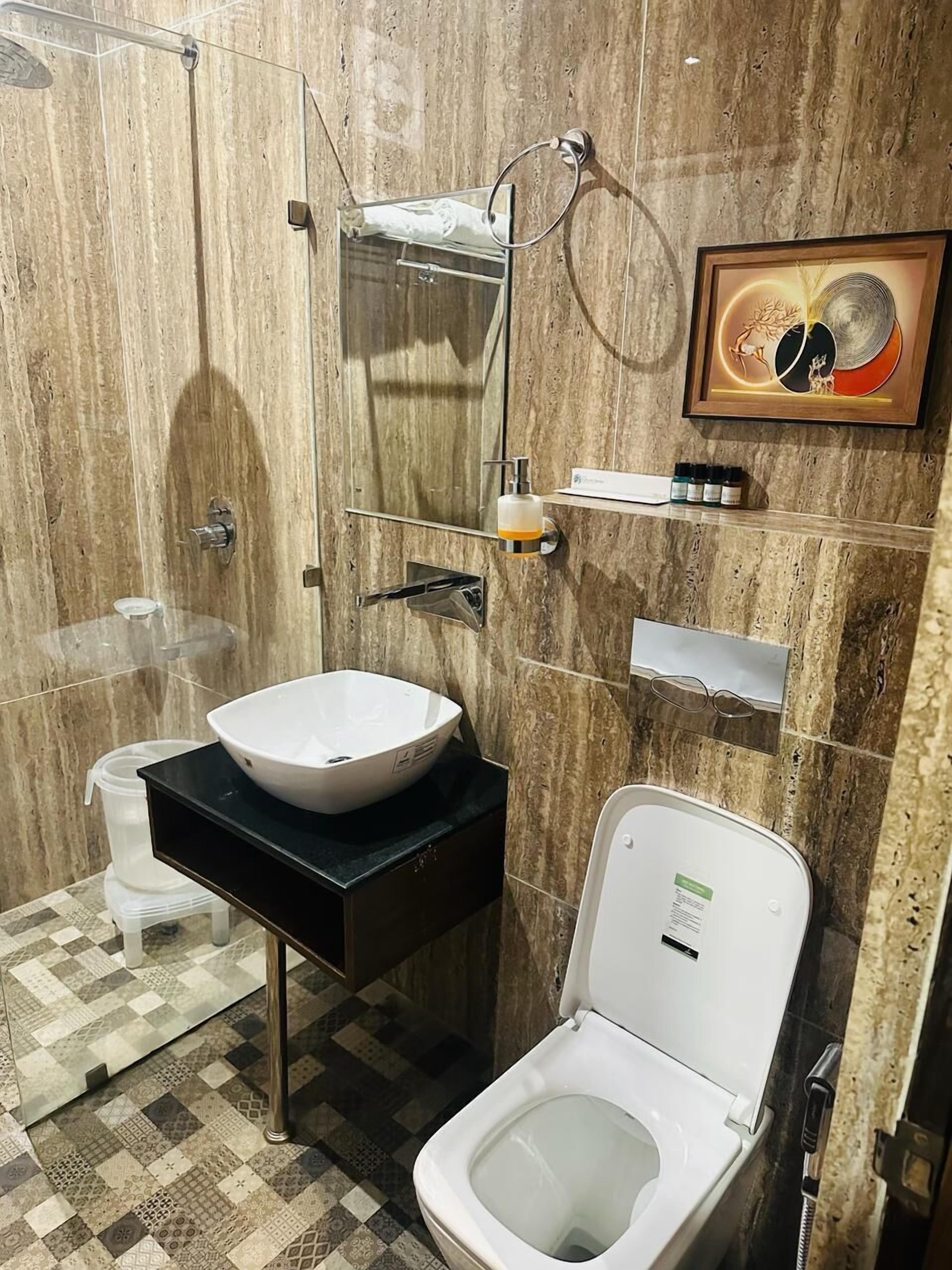 A modern bathroom with a marble wall, a white sink, a toilet, and a shower area.