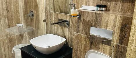 A modern bathroom with a marble wall, a white sink, a toilet, and a shower area.