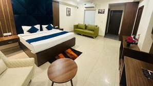 A modern hotel room with a large bed, a green sofa, a wooden side table, and a small round table. - Hotel Fortune Ganga (Haridwar)