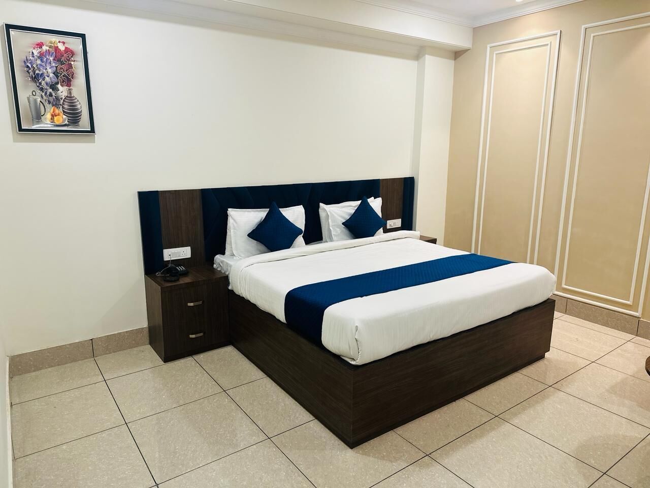 A neatly made bed with a dark headboard, a bedside table with a phone, and a wall-mounted power outlet.