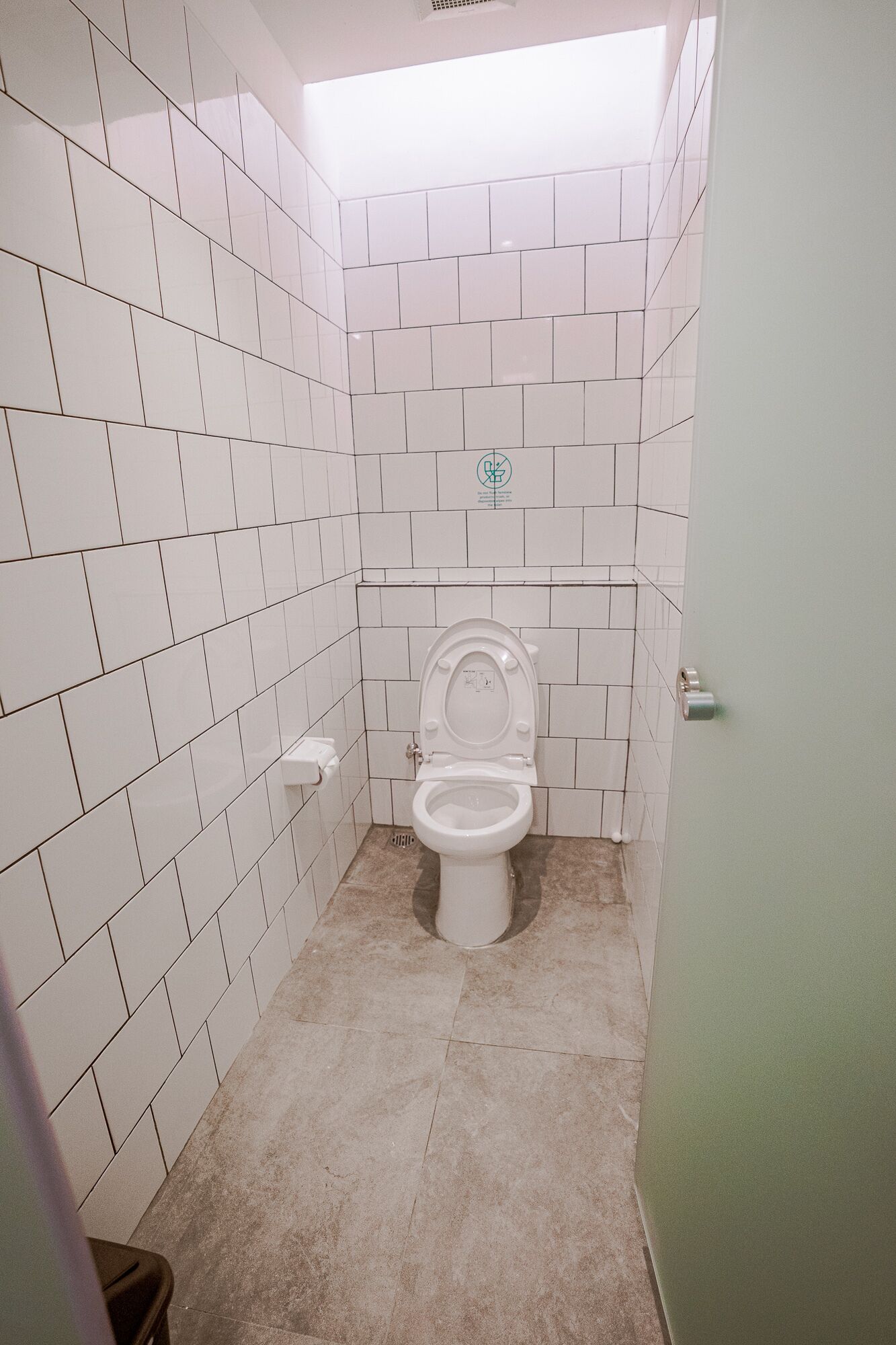 Un baño pequeño con azulejos, un inodoro, un cubo de basura y un dispensador de papel higiénico en la pared.
