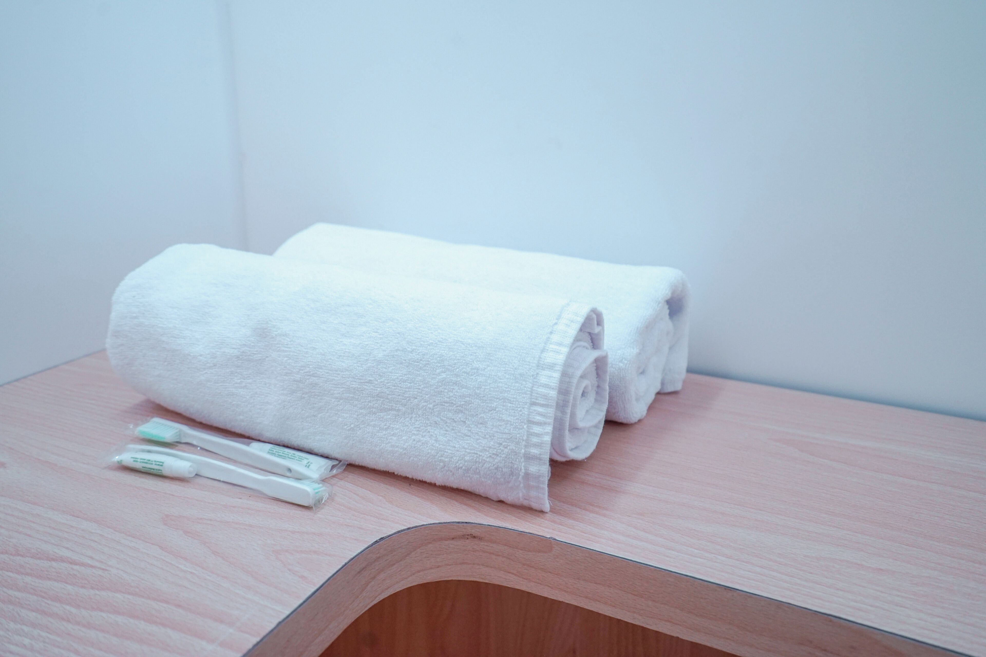 A neatly folded white towel and a toothbrush on a wooden surface in a room.