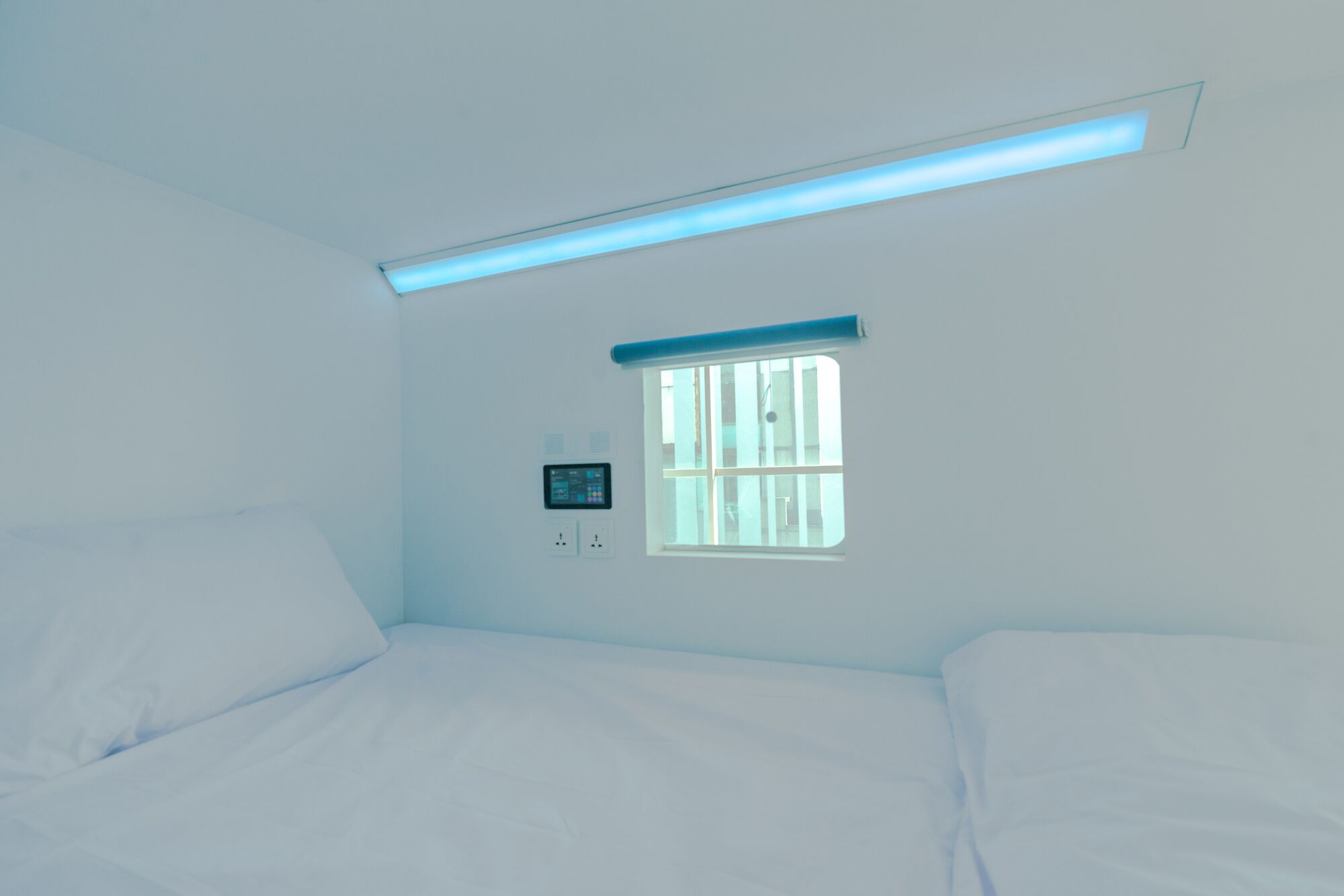 Quarto com cama, janela e painel de controle na parede.
