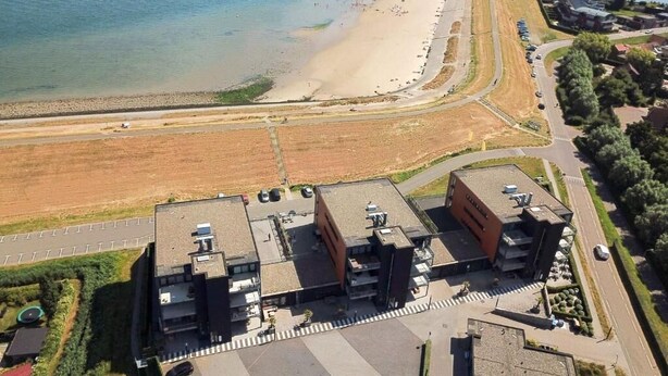 An aerial view of a coastal hotel with a parking lot, a beach, and a body of water. - Appartement Wemeldinge 06 (Wemeldinge)