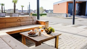 A wooden bench and table with breakfast items including croissants, juice, and a fruit bowl. - Appartement Wemeldinge 06 (Wemeldinge)