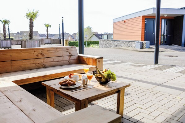 A wooden bench and table with breakfast items including croissants, juice, and a fruit bowl.