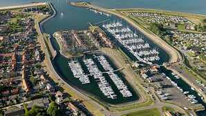 An aerial view of a marina with numerous boats docked, surrounded by residential buildings and a small commercial area. - Appartement Wemeldinge 06 (Wemeldinge)