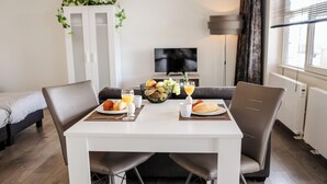 A hotel room with a dining table set for breakfast, a sofa, a TV, and a cabinet with plants. - Appartement Wemeldinge 06 (Wemeldinge)
