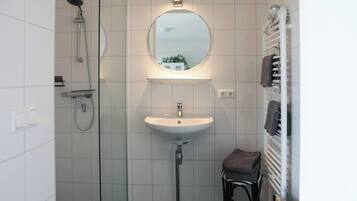 Une salle de bain avec un lavabo blanc, un miroir, un porte-serviettes et une douche.
