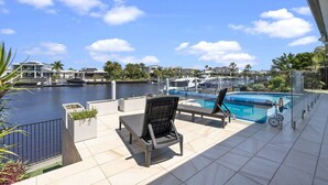 A pool area with two lounge chairs, a small pool, and a marina in the background. - Bribie Bliss: Luxe Canal Living (BANKSIA BEACH)