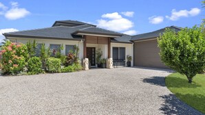 A modern house with a gravel driveway, a covered porch, and a variety of plants and shrubs around the property. - Bribie Bliss: Luxe Canal Living (BANKSIA BEACH)