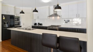 A modern kitchen with a central island, black pendant lights, stainless steel appliances, and a black and white color scheme. - Bribie Bliss: Luxe Canal Living (BANKSIA BEACH)
