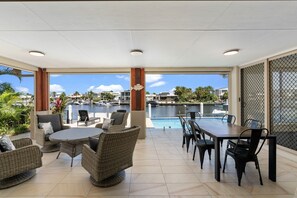 A covered outdoor area with wicker furniture, a pool table, and a view of a marina. - Bribie Bliss: Luxe Canal Living (BANKSIA BEACH)