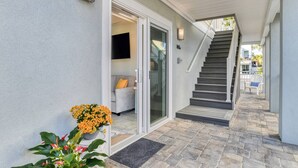 Un'area esterna coperta con una scala che conduce a un secondo piano, un ingresso con porta scorrevole in vetro e una pianta in vaso con fiori arancioni.