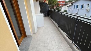 A balcony with tiled flooring, a black metal fence, and a building with a yellow facade. - Well Equipped Apartment in Bibione-beahost (San Michele al Tagliamento)