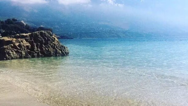 Una playa con agua cristalina y un promontorio rocoso al fondo.