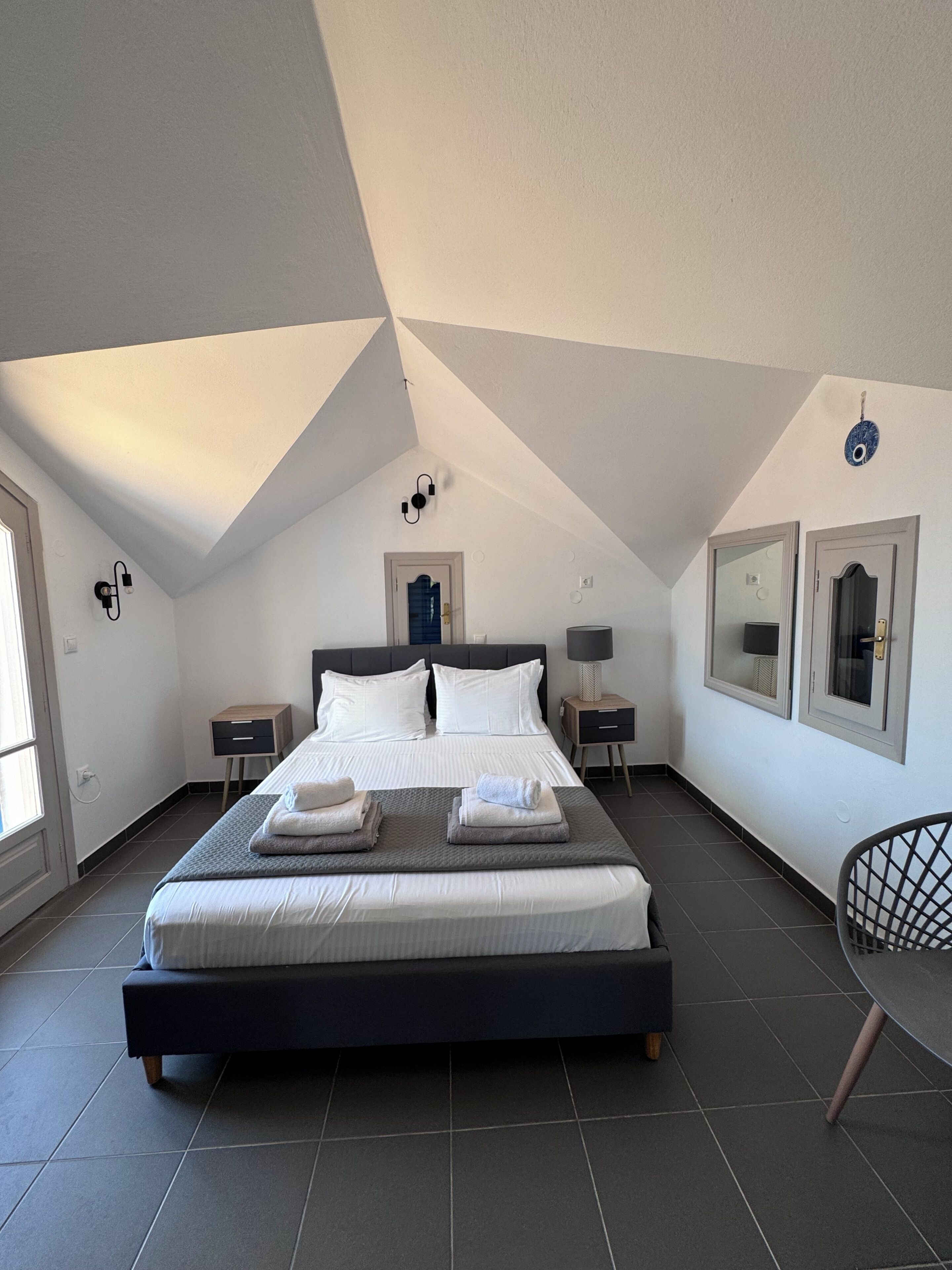 A bedroom with a large bed, two bedside tables, a chair, and a window.