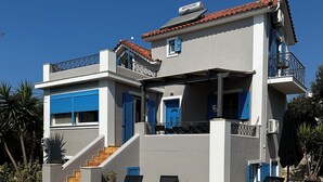 Un edificio moderno de dos pisos con piscina, contraventanas azules y un balcón con ventilador de techo.