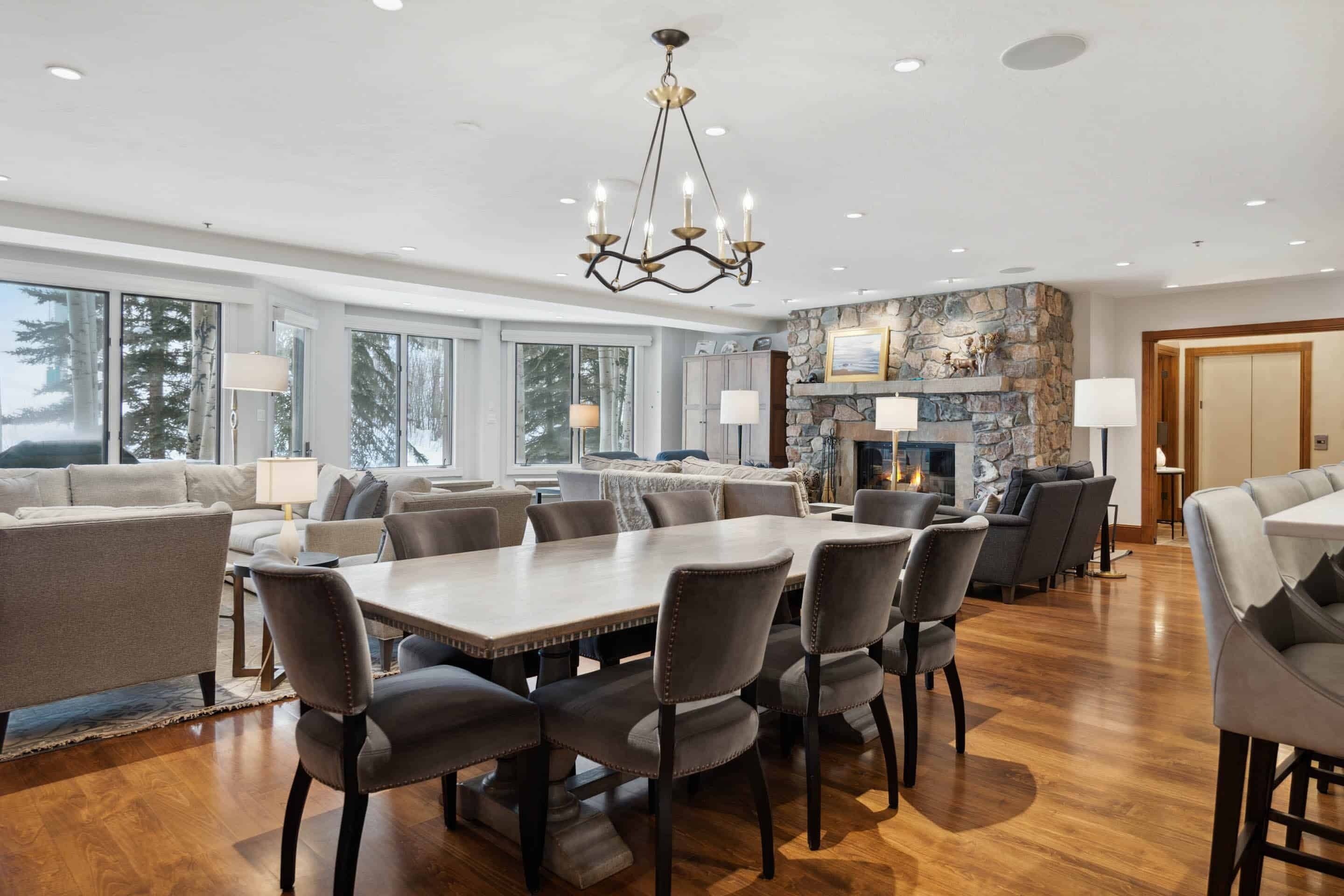 Amplia sala de estar con una gran mesa de comedor, asientos cómodos, chimenea y ventanas amplias con vistas al exterior.