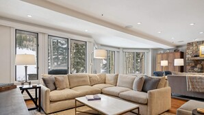 Ein geräumiges Wohnzimmer mit einem beigefarbenen Ecksofa, einem Couchtisch und einem Kamin aus Naturstein.