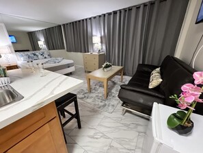 A modern hotel room with a bed, a black leather sofa, a wooden coffee table, and a small kitchen area with a marble countertop and sink. - Aloha Surf Waikiki - 5 minute walk to Waikiki beach (Honolulu)