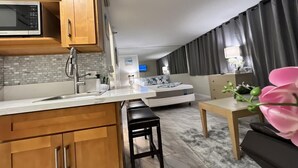 Et moderne køkken med træskabe, en mikrobølgeovn og en vask. Der er et spiseområde med et bord og stole, og en stue med en sofa og et fjernsyn.