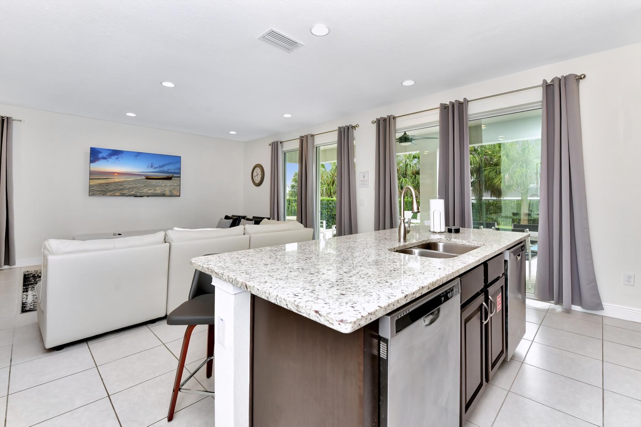 A modern kitchen with a granite countertop, stainless steel appliances, and a large window with curtains.