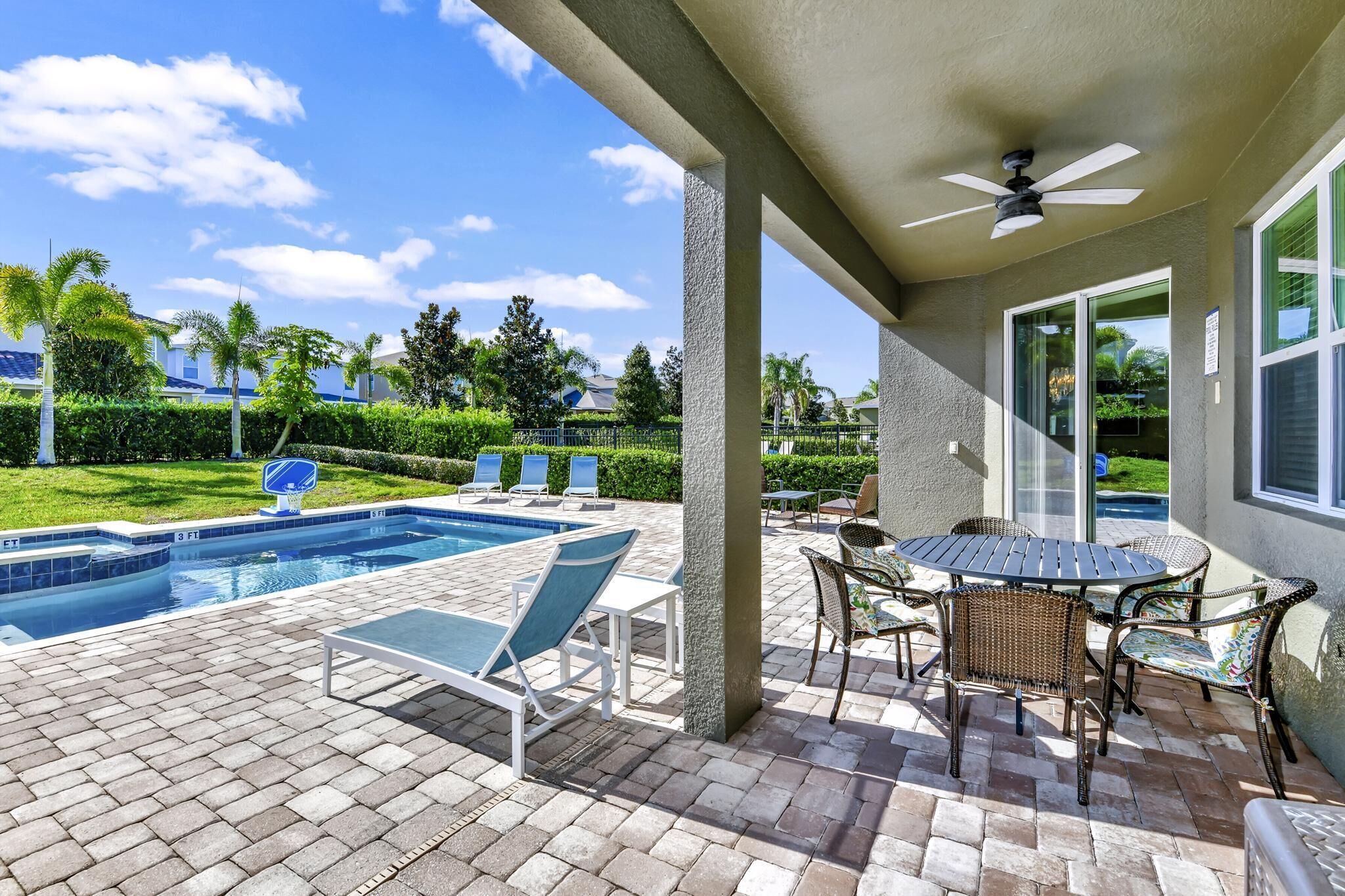 A covered outdoor area with a pool, lounge chairs, and a table with chairs.