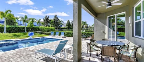 A covered outdoor area with a pool, lounge chairs, and a table with chairs.