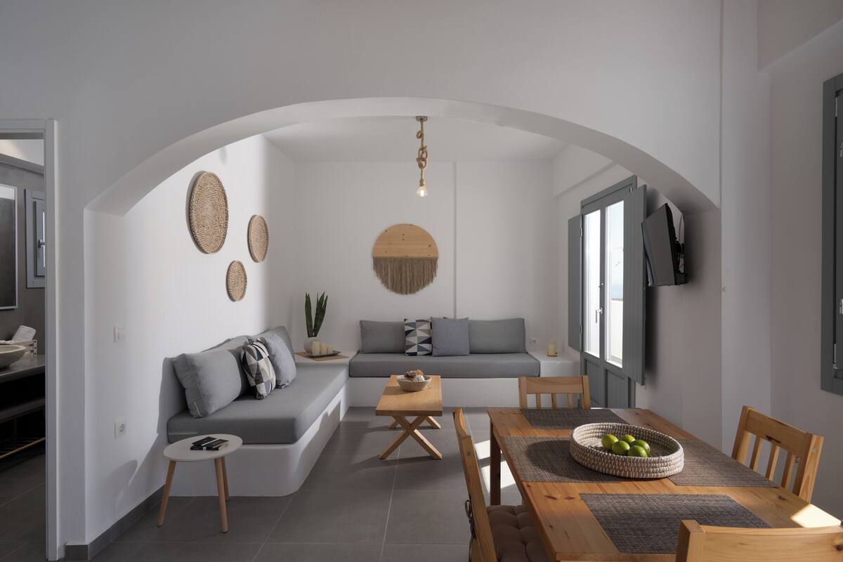 Una sala moderna con un sofá gris, una mesa de comedor de madera y una lámpara colgante.