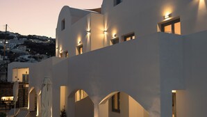 A modern building with multiple balconies, outdoor seating, and ambient lighting. - The Vine Suites (Santorini)