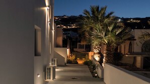 A narrow, illuminated corridor with a palm tree and a patterned floor mat. - The Vine Suites (Santorini)