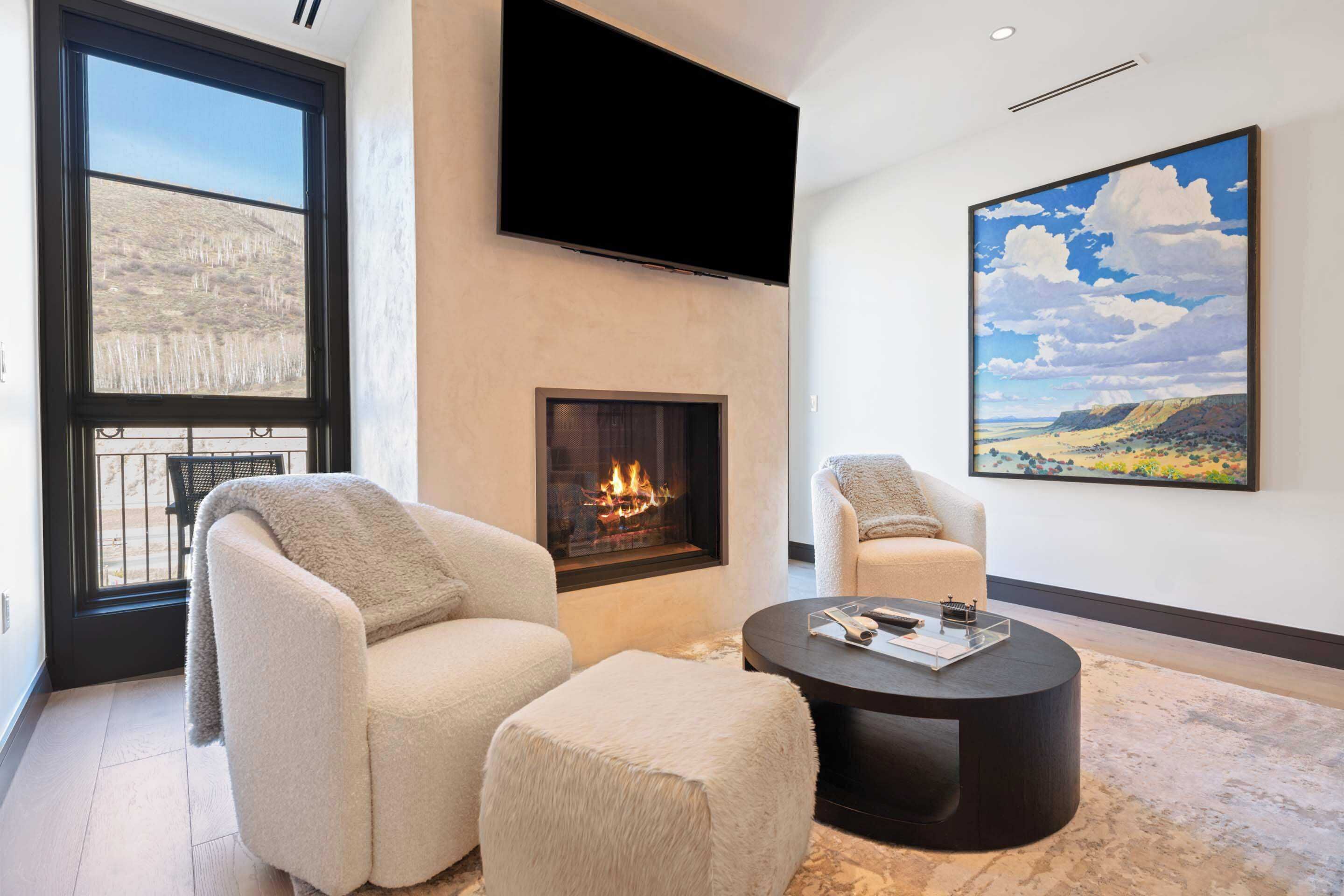 A modern living room with a fireplace, comfortable seating, and a large window.