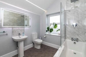 A modern bathroom with a white sink, toilet, and bathtub, marble walls, and a large mirror. - 3 Bed Pakefield Terrace | Lowestoft, Suffolk (Pakefield)