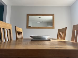 Ein Esstisch mit Schüssel und Untertasse, umgeben von Holzstühlen, mit einem Spiegel darüber.