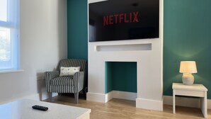 Una sala de estar moderna con un televisor de pantalla plana sobre la chimenea, un sillón a rayas, una mesita auxiliar con una lámpara y un control remoto sobre la mesa de centro.