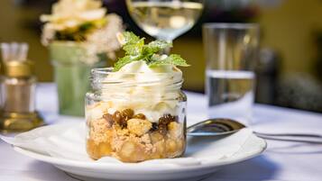 Un postre en un tarro sobre un plato blanco, con una copa de vino blanco y un vaso de agua al fondo.
