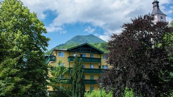 Un edificio de varios pisos con balcones, rodeado de exuberante vegetación y una montaña al fondo.