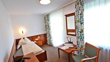 Una habitación de hotel con cama, mesita de noche, escritorio, silla y espejo.