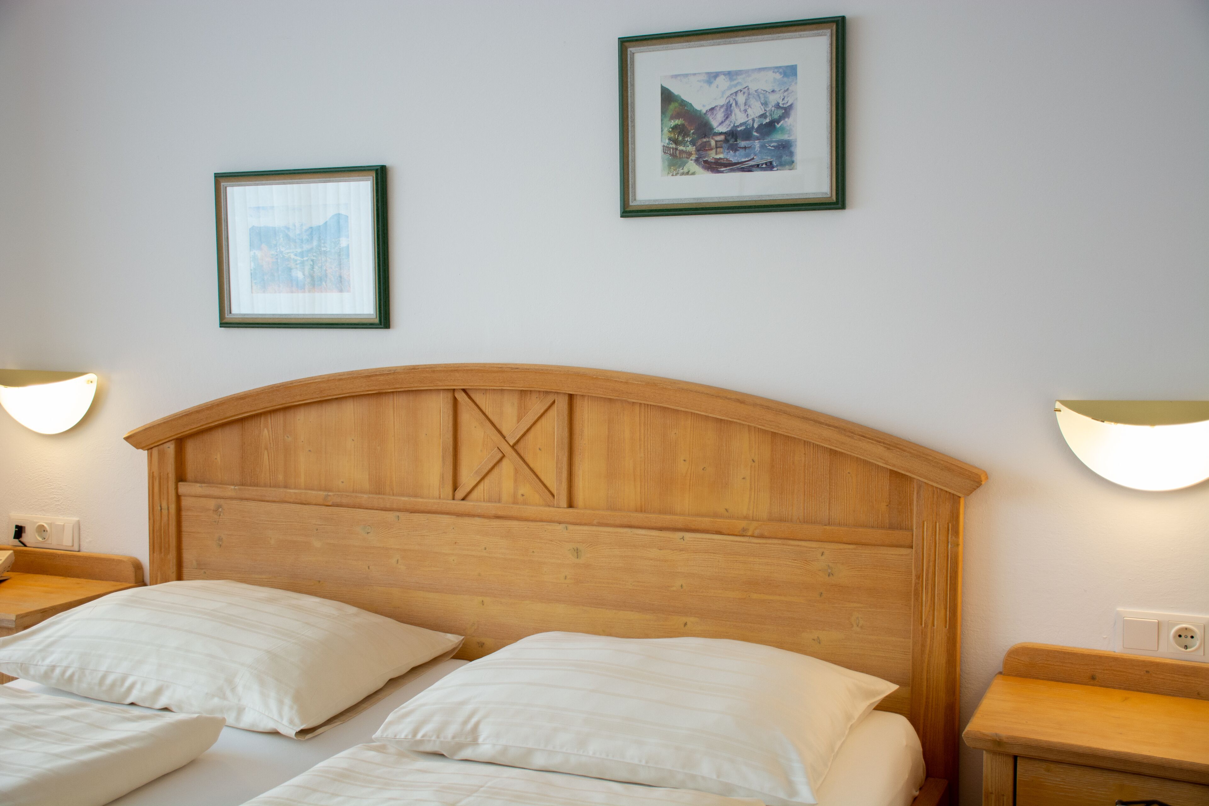 Habitación de hotel con cabecera de madera, dos camas, lámparas de noche y dos cuadros en la pared.