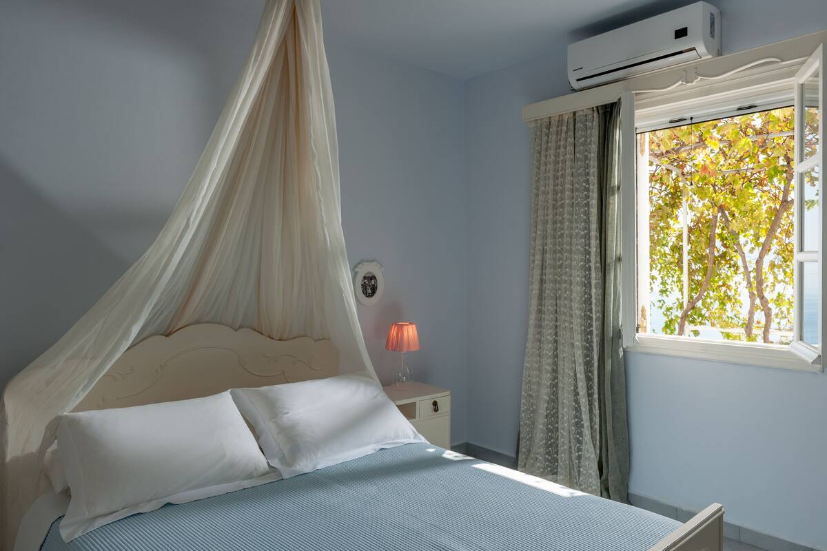 A bedroom with a canopy bed, bedside lamp, and a window with a view of trees.
