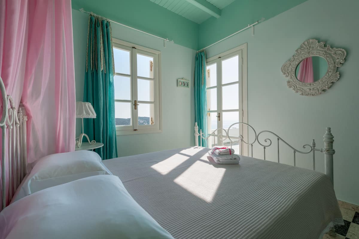 A bedroom with a bed, curtains, a mirror, and a window.