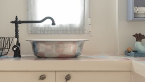 Une cuisine avec un évier de style rétro, une fenêtre ornée de rideaux légers et un mur recouvert de carreaux.